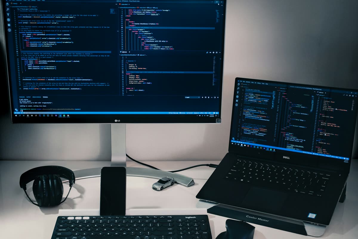 A monitor and a laptop showing source code on a white desk with headphones