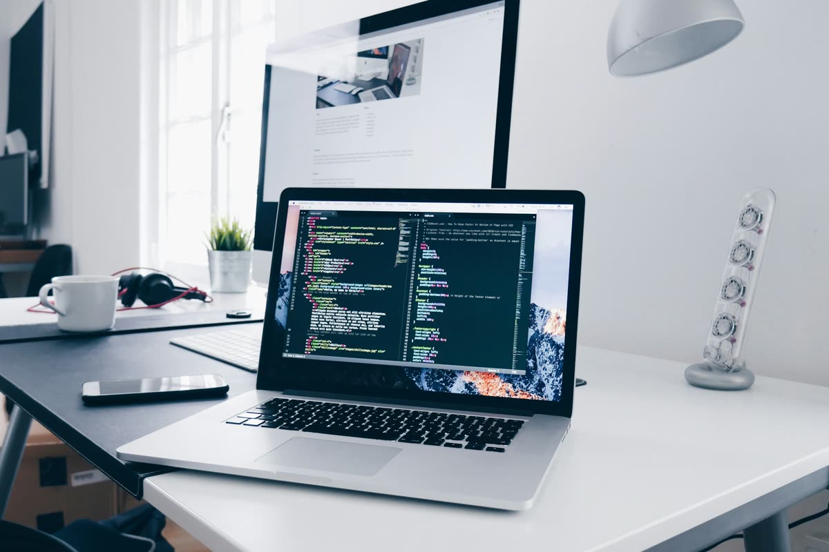 A laptop showing code on a white desk in a bright office