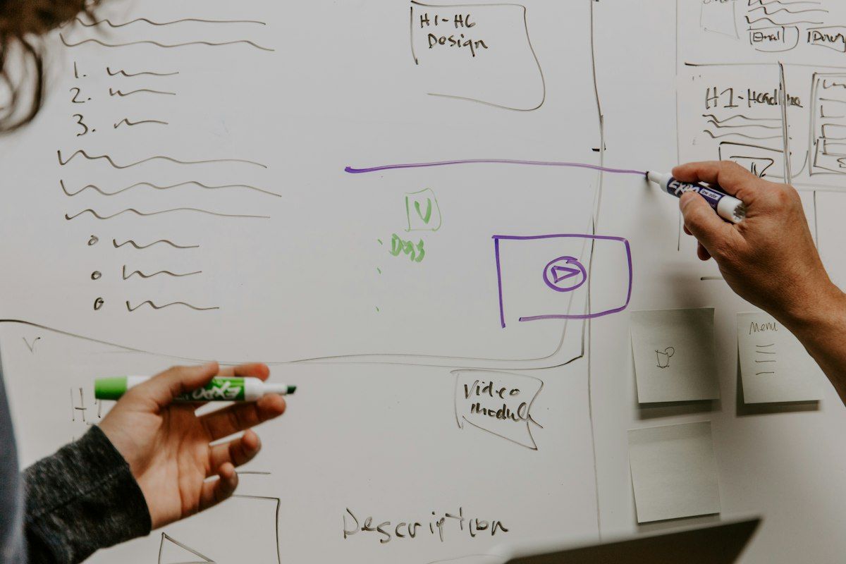 Person sketching app screens and notes on a whiteboard with a marker